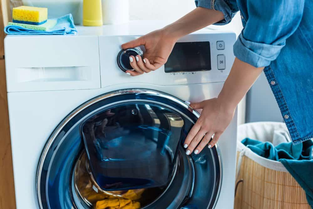 Cropped shot of woman using washing machine at home